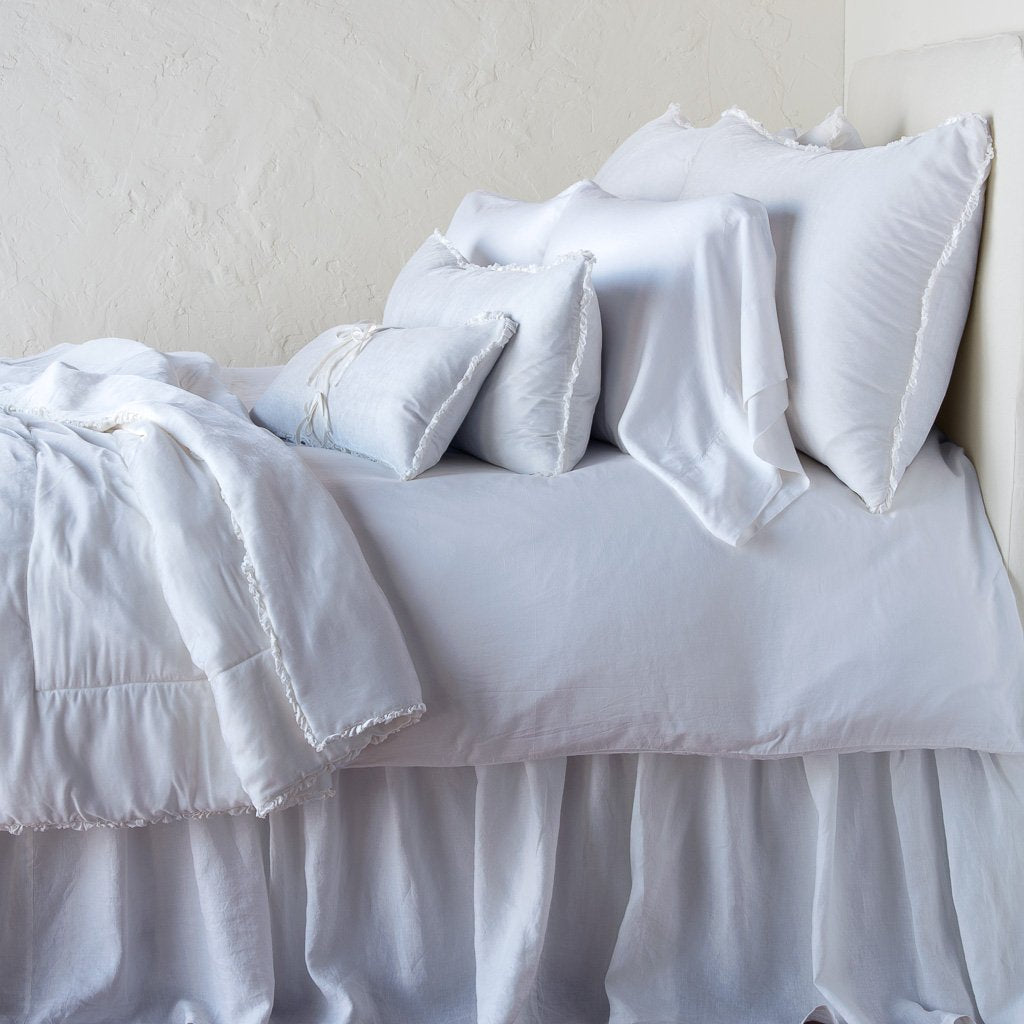 White: Silk velvet throw blanket with petite ruffle, draped across a monochromatic bed - side view.