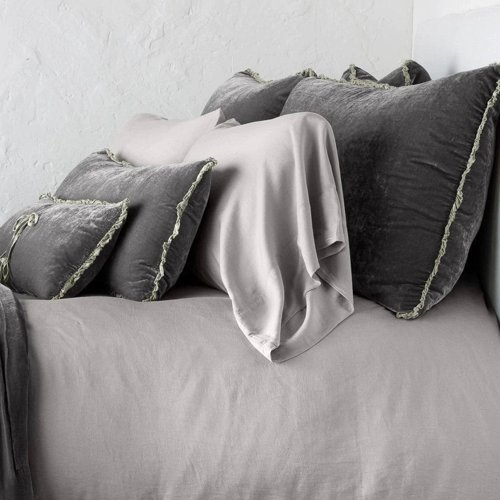 Fog: Silk velvet shams with a petite ruffle on monochromatic bed, leaning upright behind sleeping and throw pillows - side view.