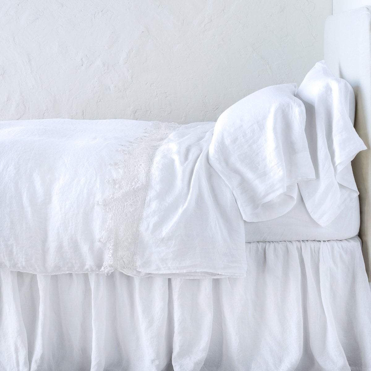 White: Lace trimmed linen flat sheet folded back over monochromatic linen bed - side view. 