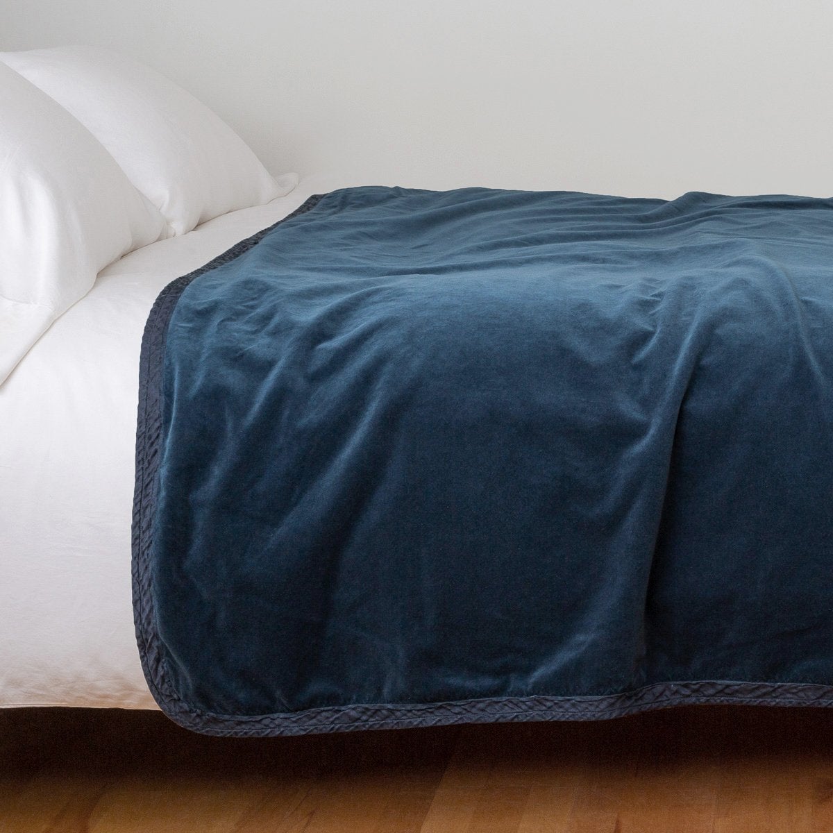 Midnight: Cotton velvet bed end sized blanket, draped on a white bed - side view.