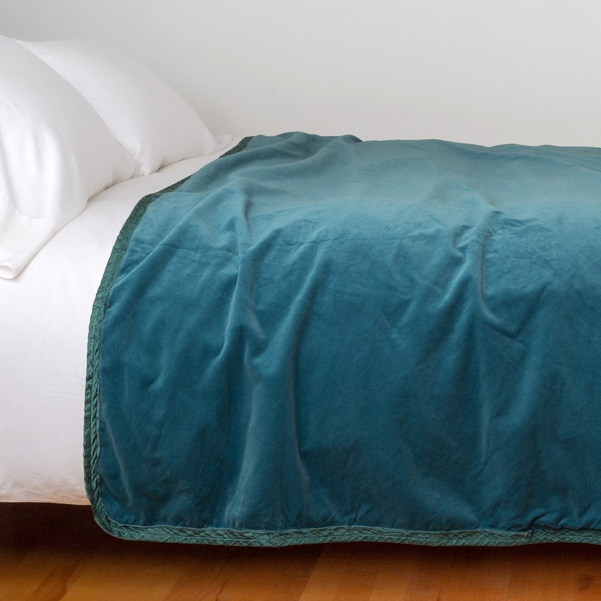 Cenote: Cotton velvet bed end sized blanket, draped on a white bed - side view.