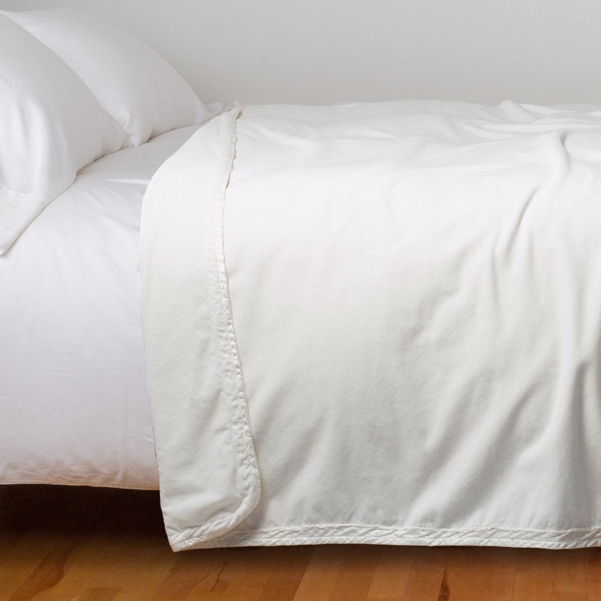 Winter White: Cotton velvet bed end sized blanket, draped on a white bed with corner folded back - side view.