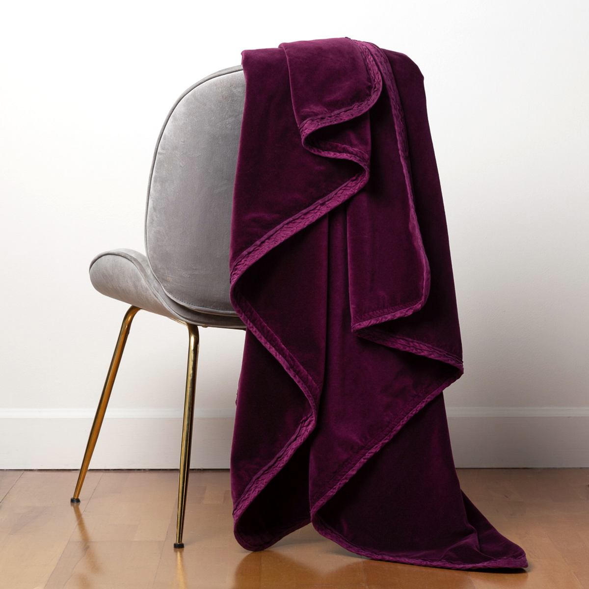 [allvariants]: Harlow throw blanket in fig draped over the back of a light grey chair, against a white wall and wood floor.