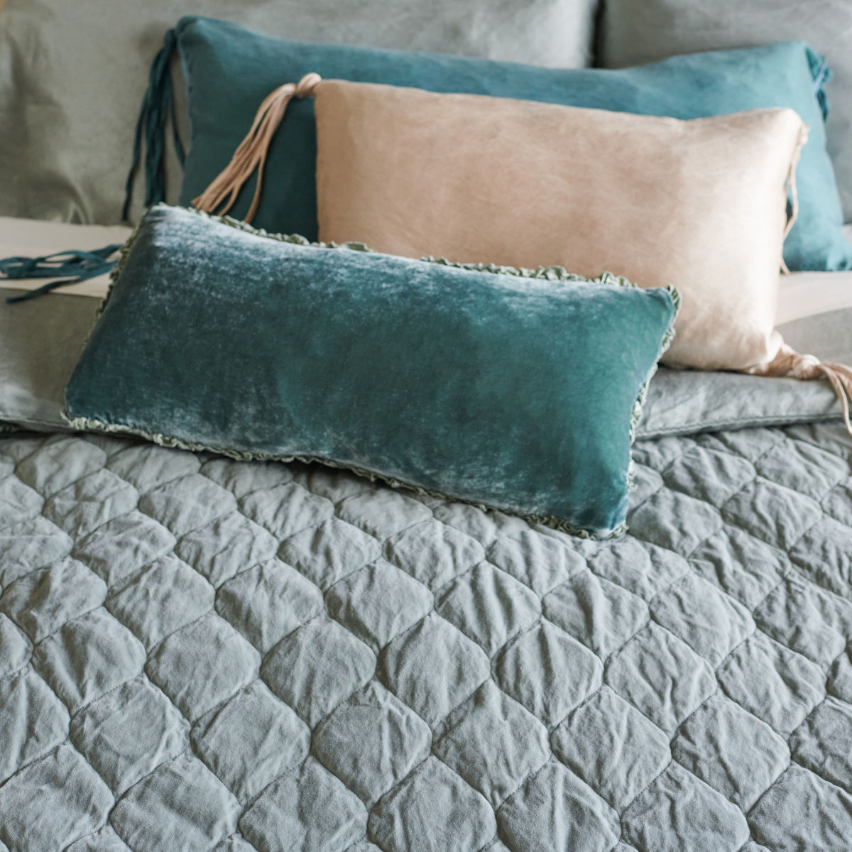 [allvariants]: Silk velvet and silk charmeuse throw pillows on a Harlow coverlet demonstrate how cotton velvet aborbs dye more subtly than vibrant silk blends - angled overhead view.