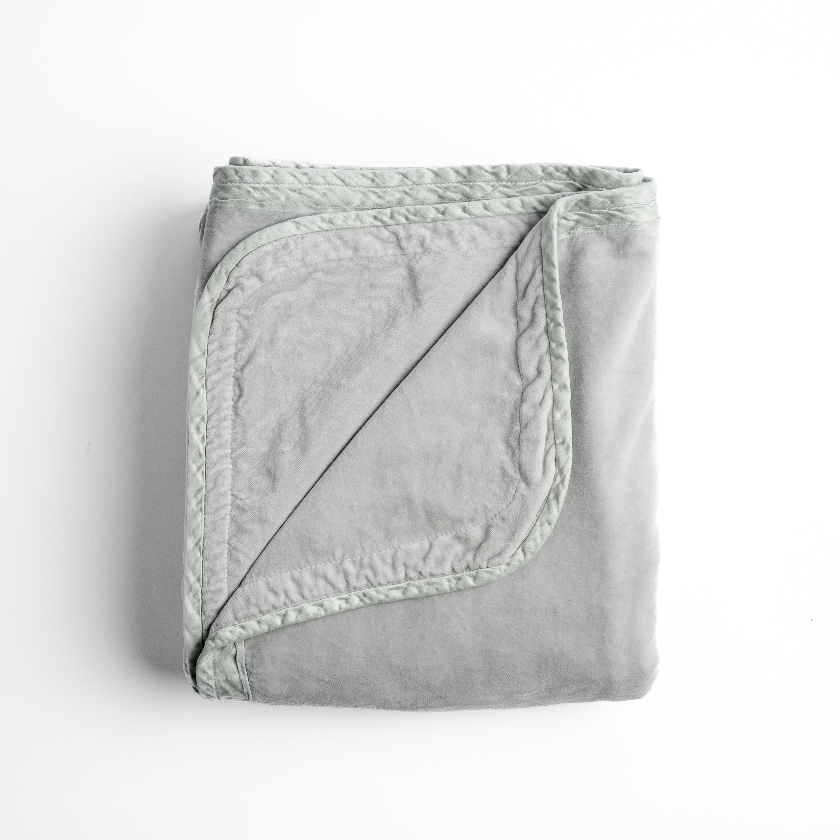 Cloud: overhead angle of the folded blanket with a corner pulled back to show the reverse and trim. 