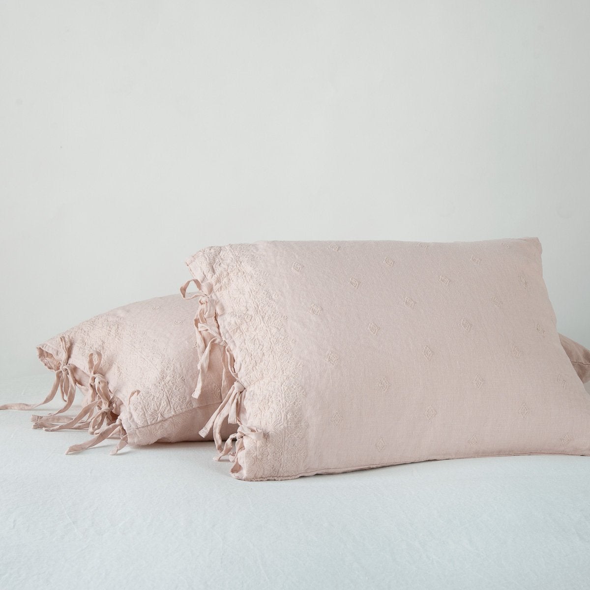 [allvariants]: Ines pearl standard sham leaning against a king sham, on a plain background and at a slight angle to showcase the linen side-tie closure.