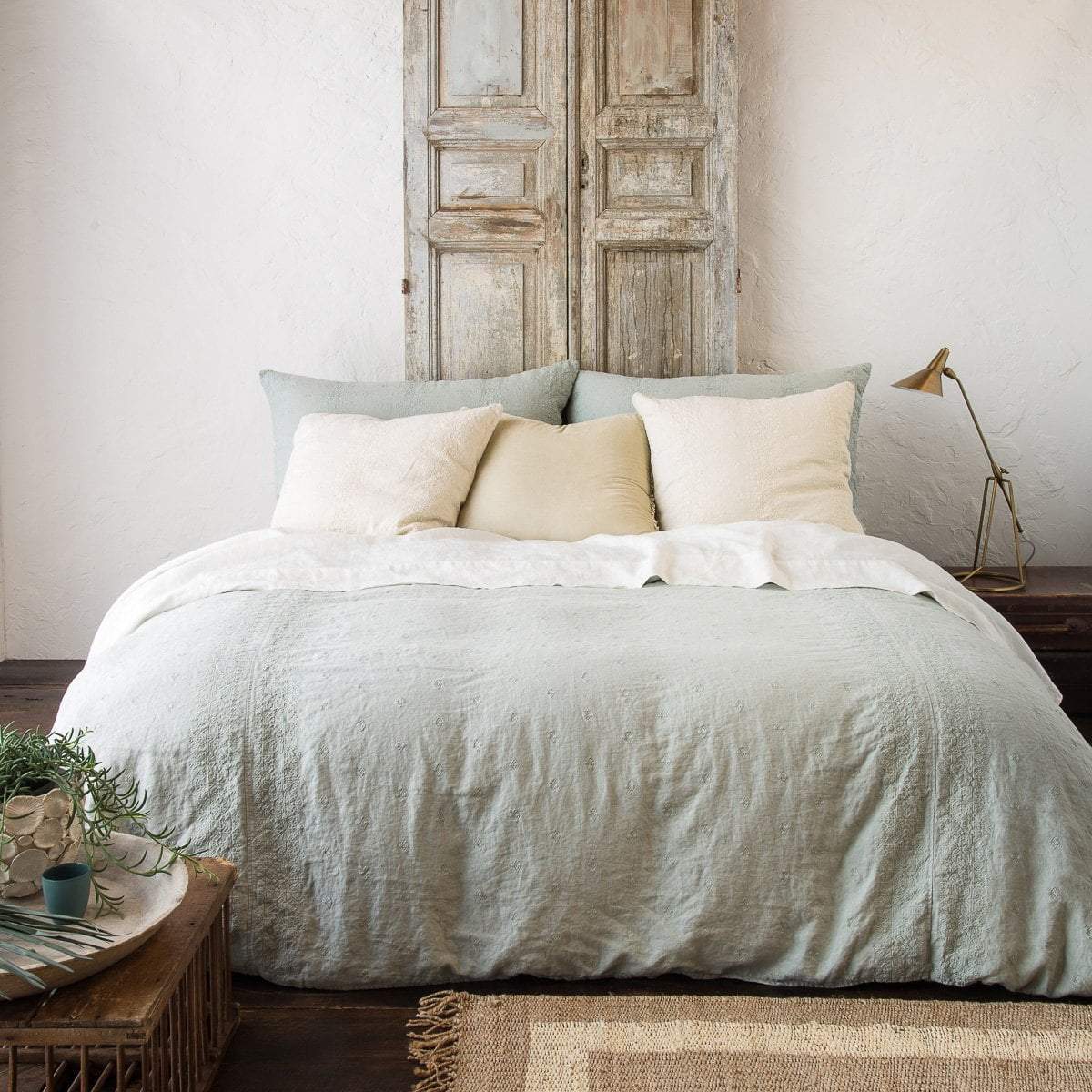 [allvariants]: Ines duvet cover in eucalyptus with cream-toned sheets and pillows, in a room with distressed wood, light walls, and neutral accents - end of bed view.