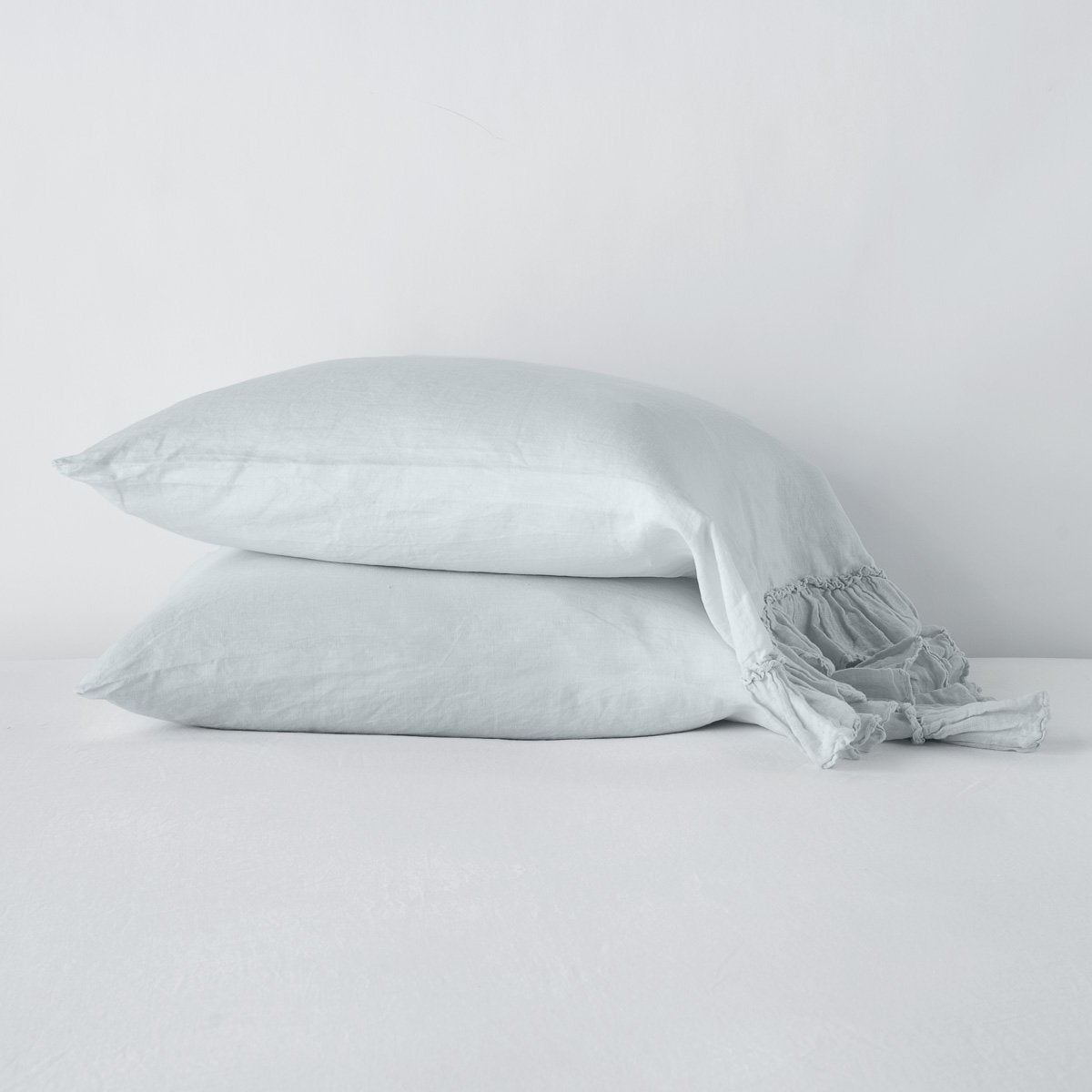 Cloud: Two sleeping pillows stacked at a slight angle against a plain background, showcasing ruffle trim detail - side view.