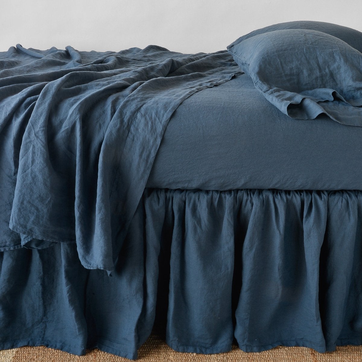 [allvariants]: Linen bed skirt in midnight, with matching rumpled sheets and sleeping pillows - side view.