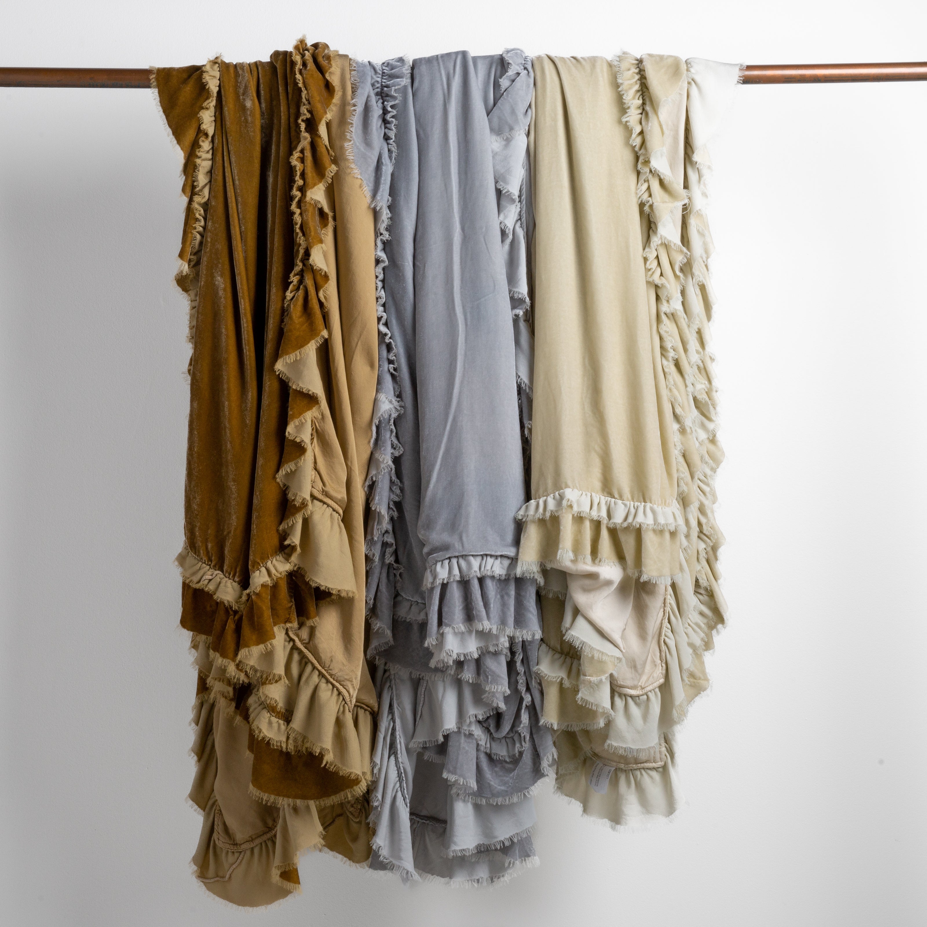 [allvariants]: three silk velvet blankets in honeycomb, sterling and parchment draped over a copper bar straight on against a white background. 