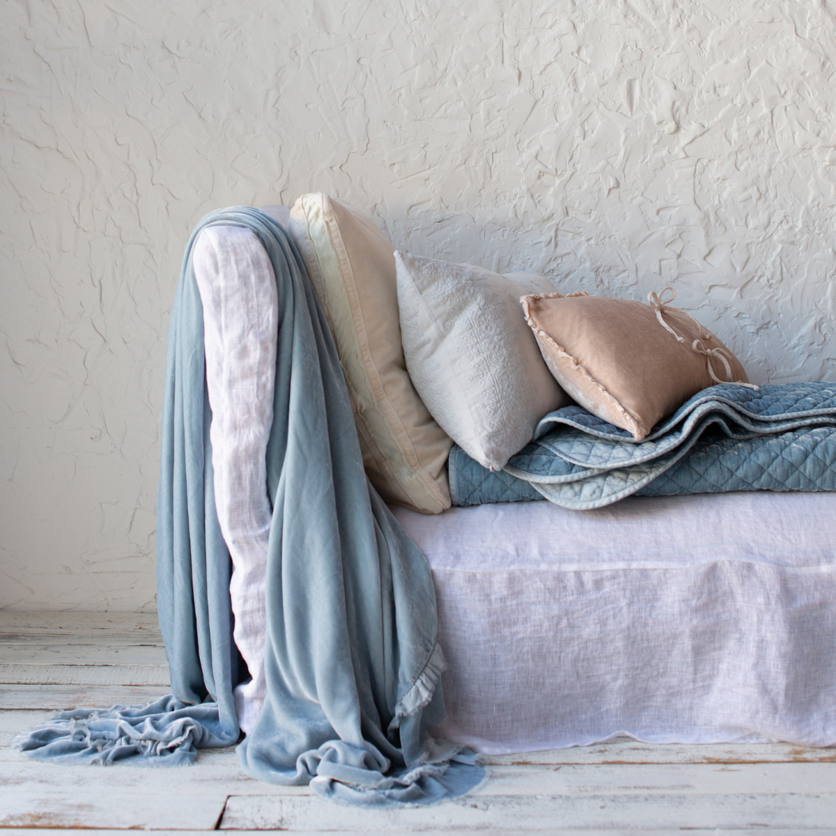 : Loulah throw blanket in cloud, draped over the side of a white linen day bed sofa, layered with light neutral pillows in a variety of textures.