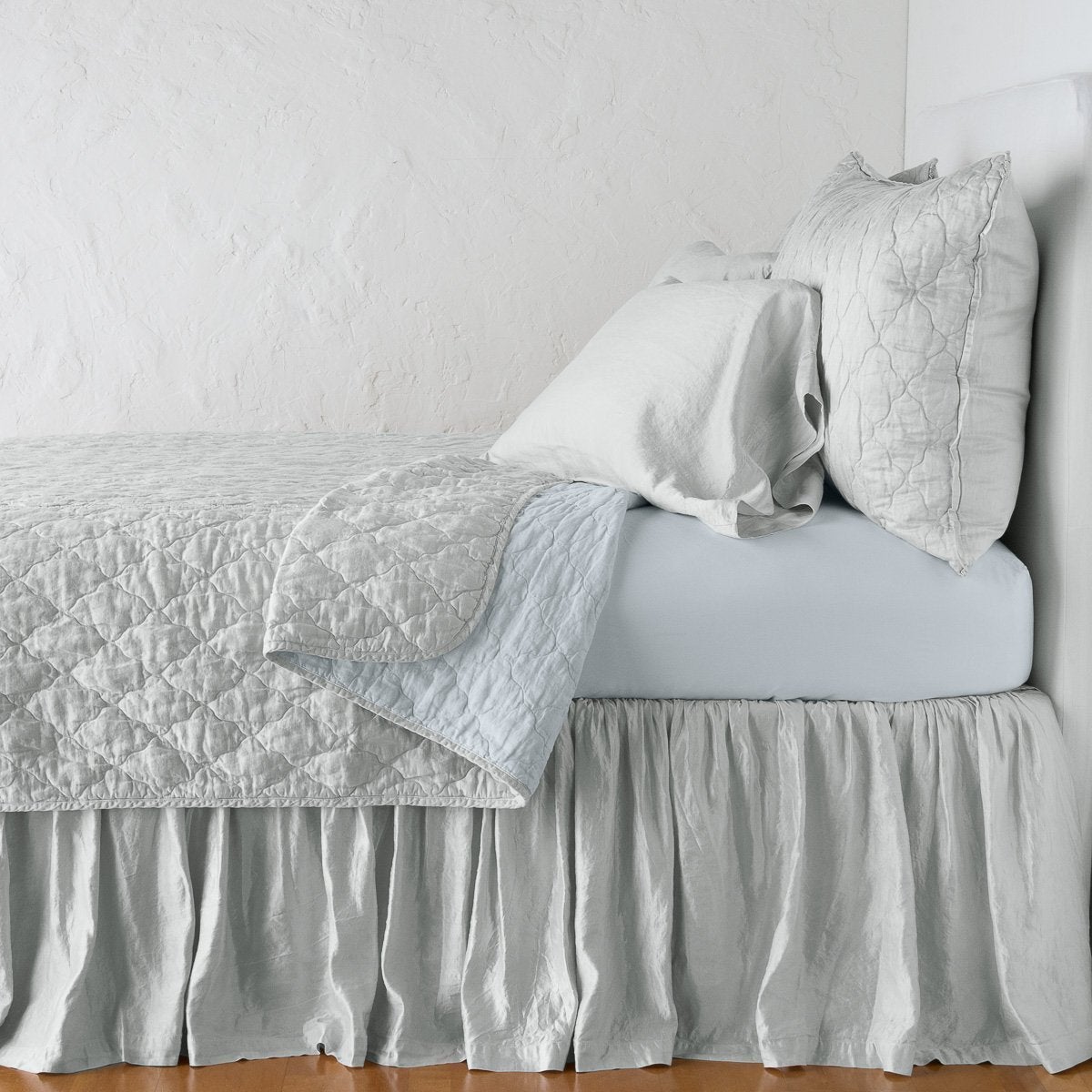 Cloud: coverlet neatly folded back to reveal linen reverse, on a monochromatic bed - side view.