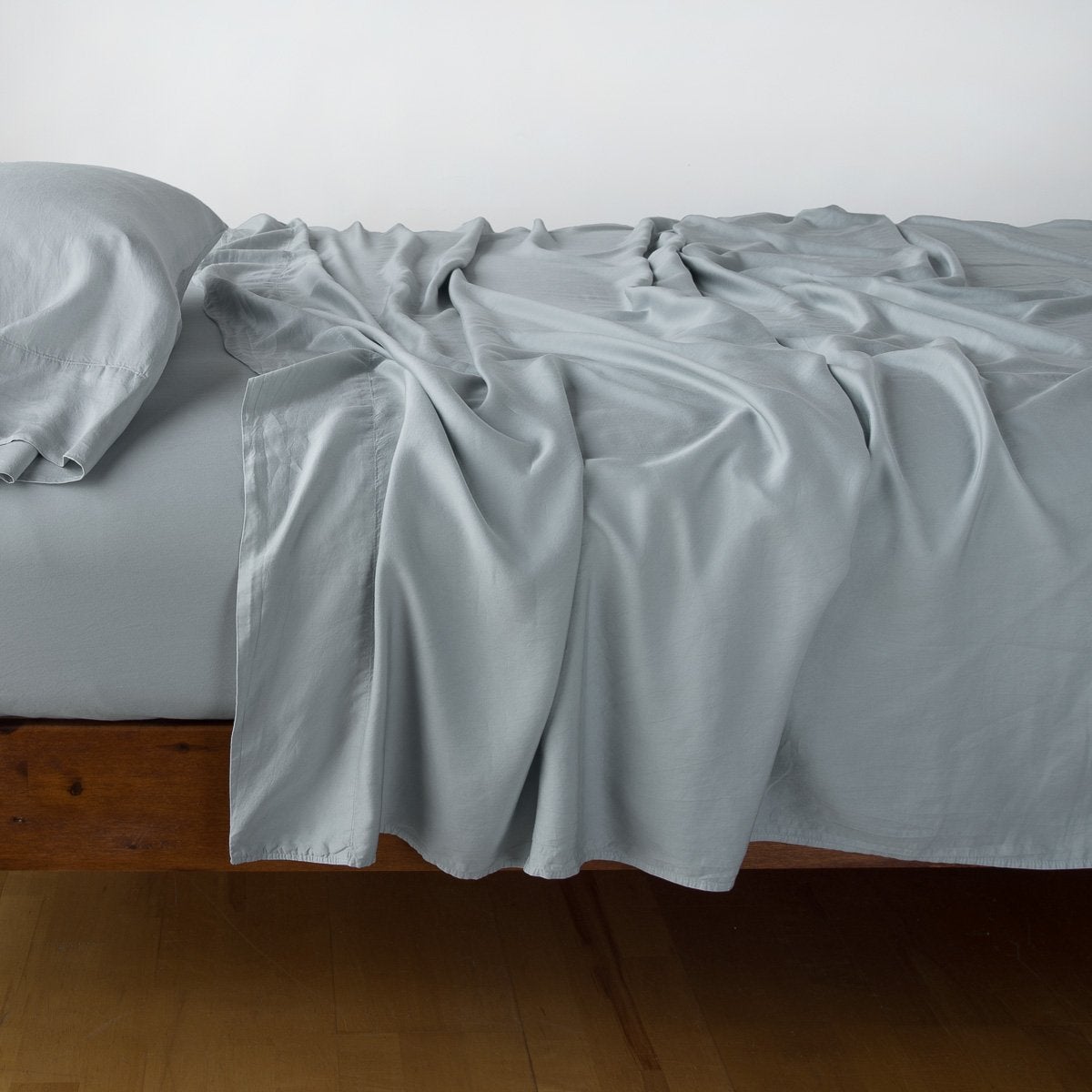 : Madera Luxe fitted sheet with matching rumpled flat sheet and sleeping pillow - mineral, side view.