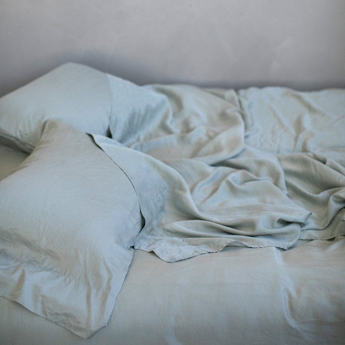 [allvariants]: Rumpled Madera Luxe sheeting with matching sleeping pillows - mineral, slightly overhead side view.