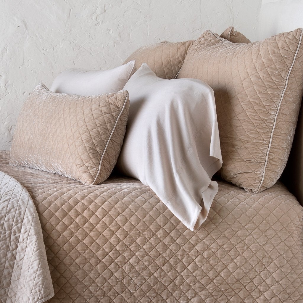 [allvariants]: Silk velvet quilted shams layered with matching coverlet and lumbar and on-tone sleeping pillows, all in pearl - cropped side view.