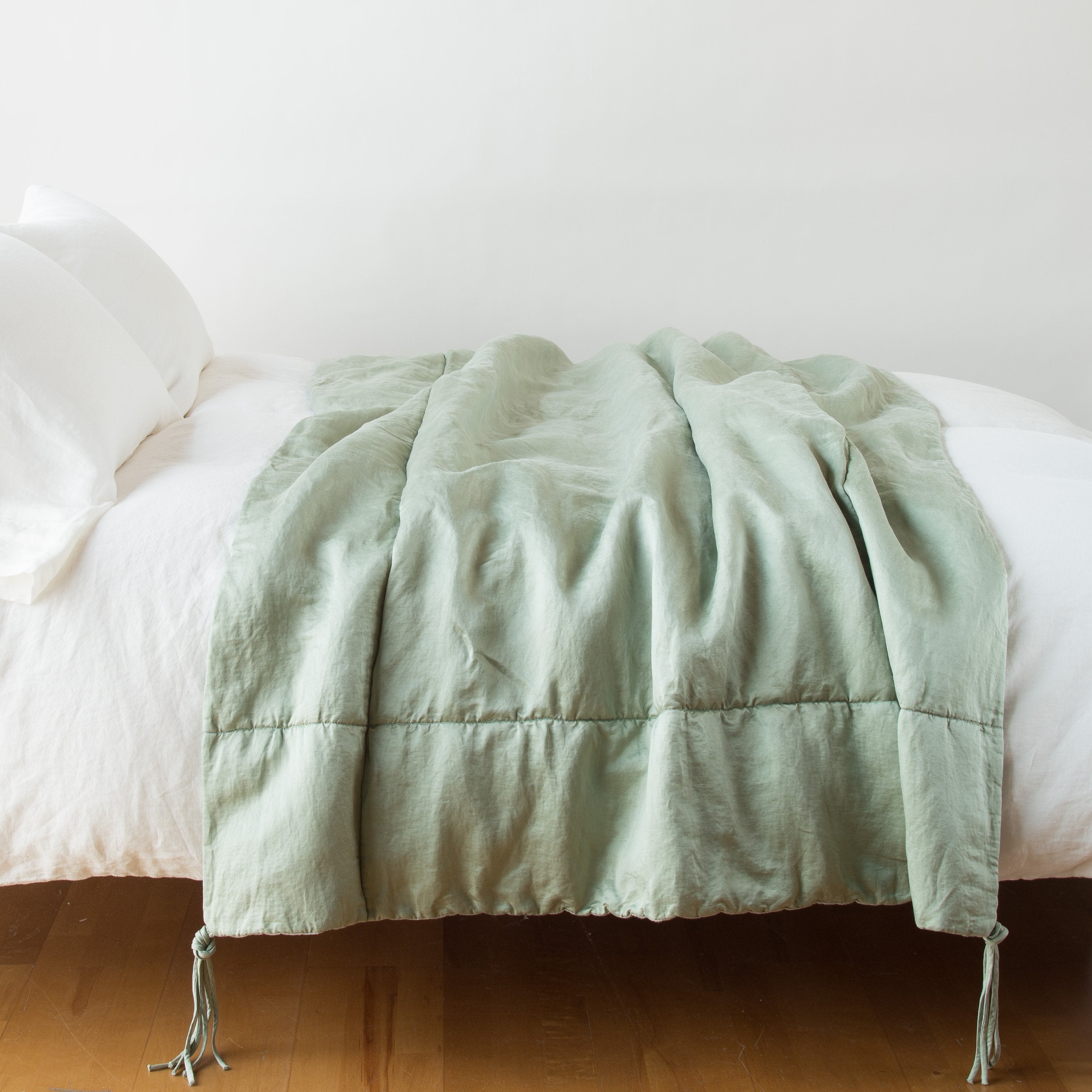 Eucalyptus: Taline throw blanket draped over a white bed - eucalyptus, side view.