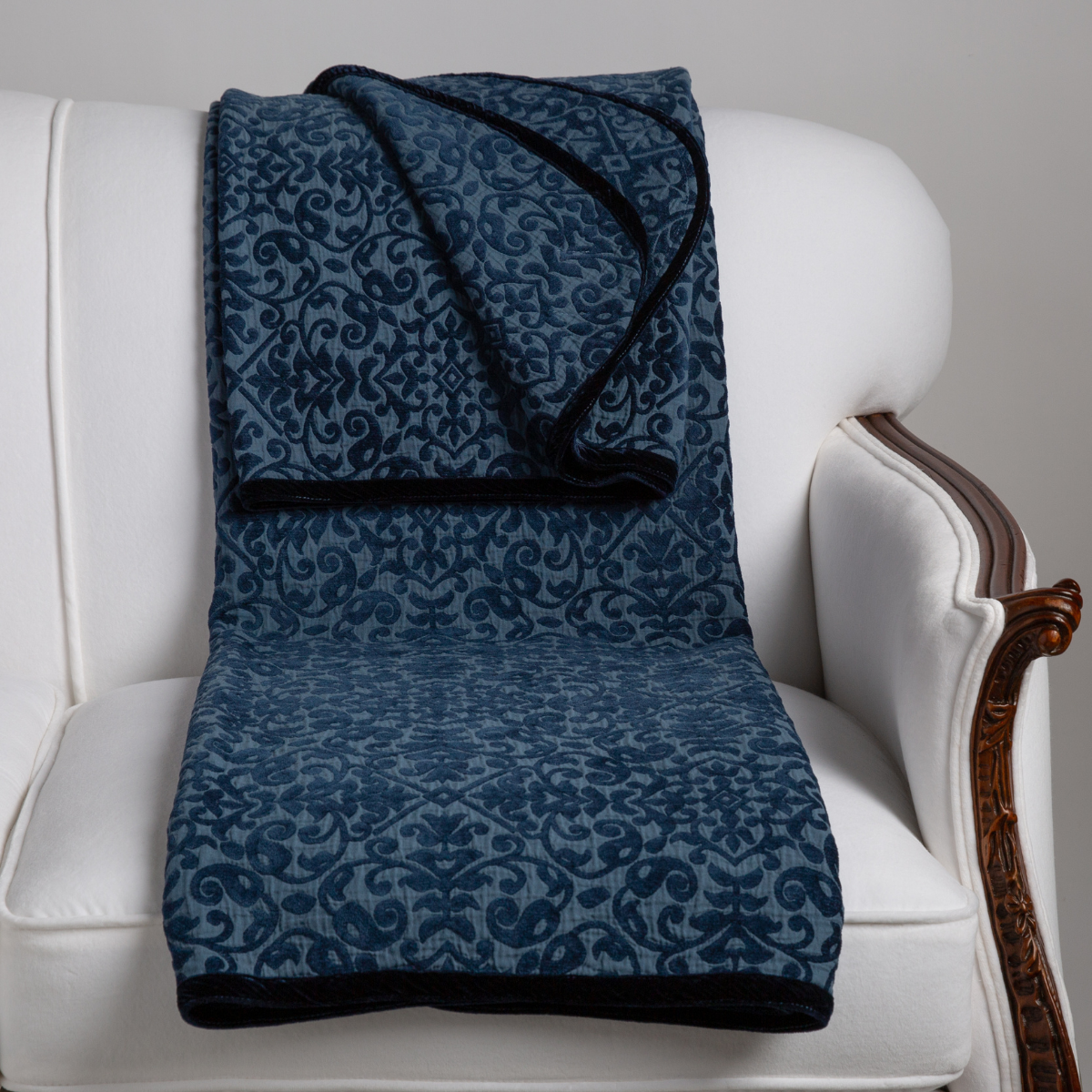 Midnight: The blanket is neatly folded with its corners turned back showing the trim. Blanket is carefully draped on a white sofa with wood detailing. 