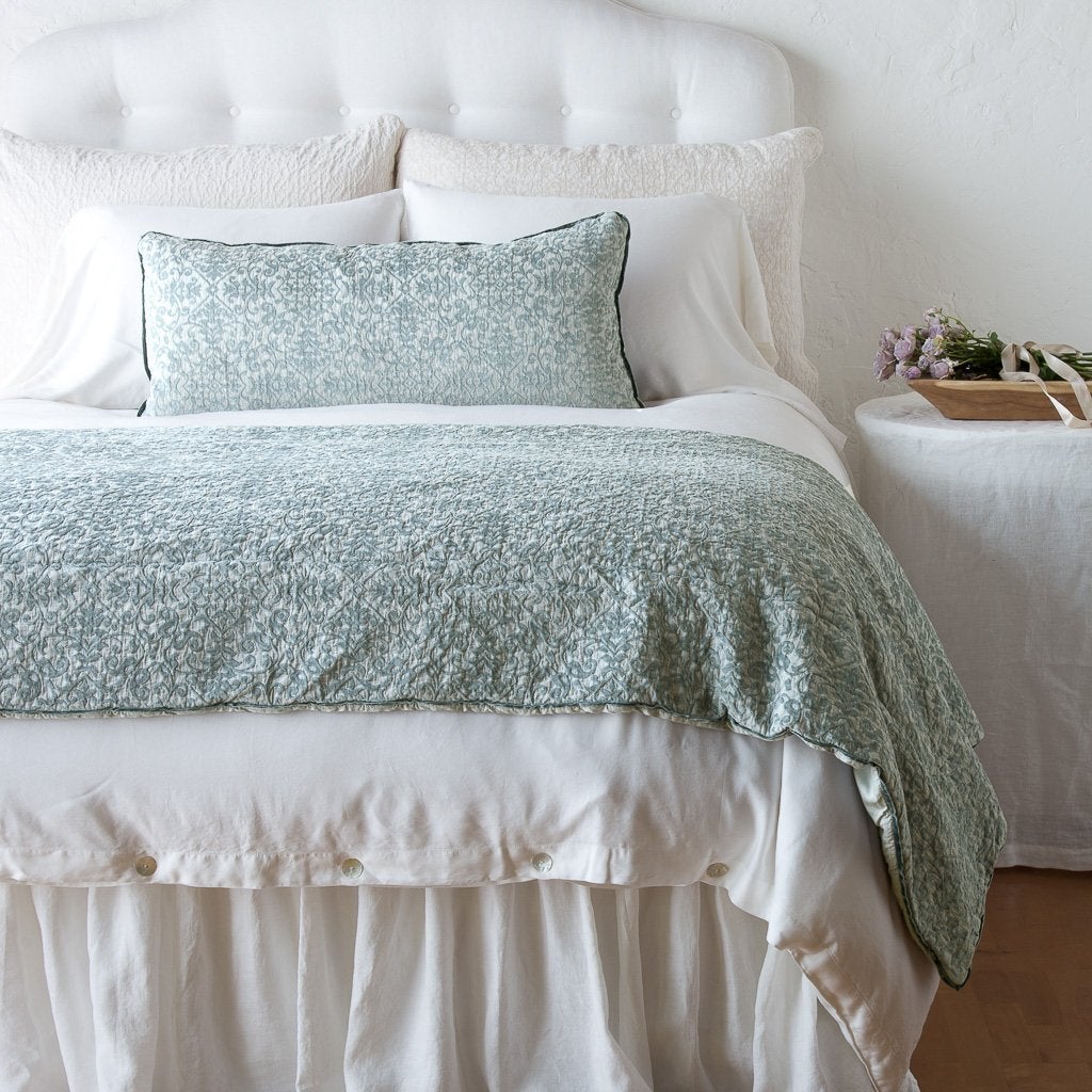 : Vienna 16x36 pillow and matching throw blanket on a white, neatly made bed - eucalyptus, end of bed view.
